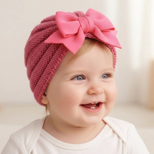 Détail d'un bonnet tricoté pour bébé avec un grand nœud en satin rose et maille