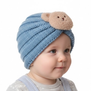 Close-up detail of blue knitted baby turban featuring a cute plush bear decorative patch