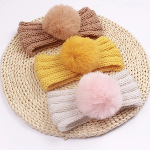 Close-up of knit baby headbands with faux fur pom poms in brown, yellow and pink colors