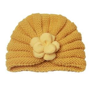 Detail der gelben Strickmütze für Babys mit einer 3D-Stoffblume auf weißem Grund