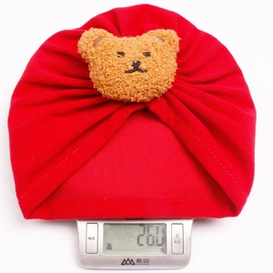 Detail showing the lightweight 26g red cotton baby turban hat with cute teddy bear patch