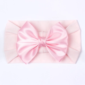 Gros plan d'un bandeau rose pour bébé avec un grand nœud en satin soyeux sur fond blanc