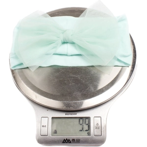 Detailed view of lightweight mint green mesh bow baby headband on a digital scale