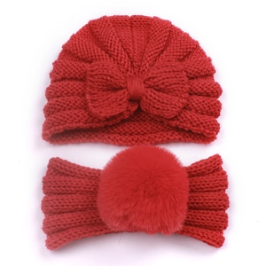 Detail of red knitted baby set featuring a soft bow beanie and a faux fur pompom headband
