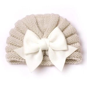 Gros plan d'un bonnet de bébé en tricot beige avec un grand nœud blanc sur fond blanc