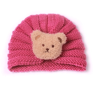 Close-up of deep pink knitted baby turban hat with a cute brown plush bear decoration