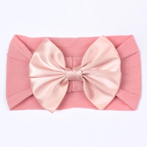 Détail du bandeau élastique rose bébé avec grand nœud en satin sur fond blanc