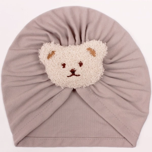 Detailed view of mauve baby knit turban hat featuring a plush teddy bear patch decoration