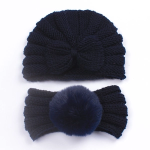 Flat lay detail of navy blue knitted baby hat and headband set with a faux fur pompom