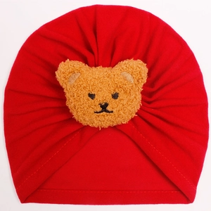 Detailed close-up of a red knit baby beanie featuring a soft brown plush bear ornament