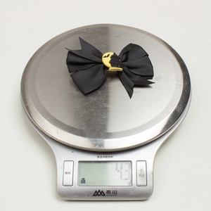 Detail showing a 4.3g Halloween bow hair clip with bat and moon charm on a scale