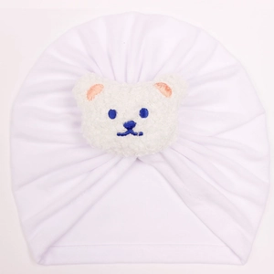 Close-up of baby white turban hat featuring soft pleated fabric and a plush bear detail