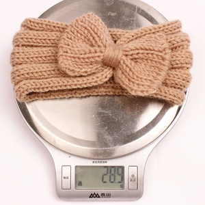 Brown knit baby headband with bow knot shown on a scale to display 28.9g weight