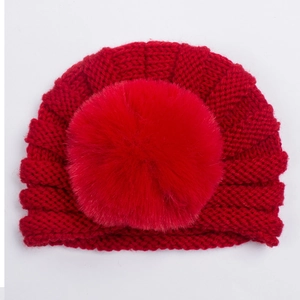 Détail d'un bonnet turban tricoté rouge pour bébé avec un pompon en fausse fourrure