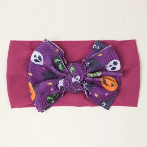 Detail of baby headband with a purple pumpkin print bow on stretchy rose pink fabric