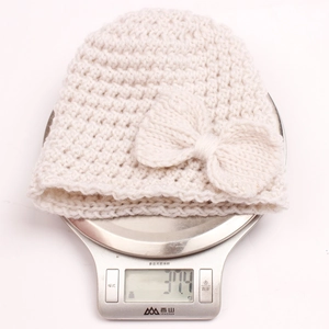 Detailed view of lightweight 37g beige knitted baby hat with bow on digital scale