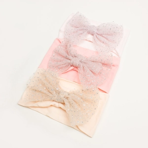 Detailed macro shot of three glittery mesh bow headbands in soft pink and apricot tones