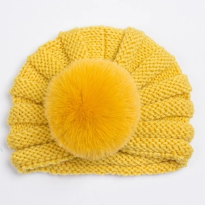 Gros plan détaillé du bonnet turban jaune pour bébé avec un grand pompon en fausse fourrure