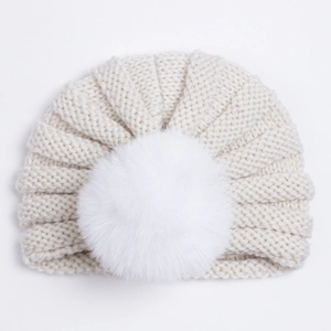 Gros plan d'un bonnet turban tricoté pour bébé avec un pompon en fausse fourrure blanche