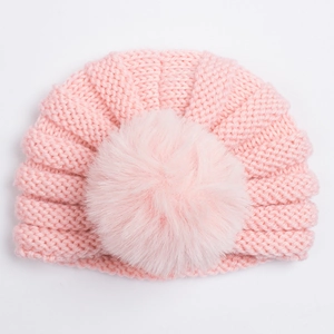 Détail du bonnet tricoté rose pour bébé avec torsades et un grand pompon en fausse fourrure