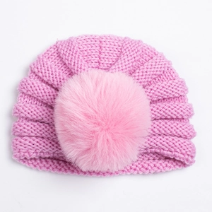 Détail du bonnet en maille rose vif pour bébé avec pompon en fausse fourrure et nœud torsadé