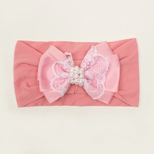 Détail d'un bandeau élastique rose pour bébé avec un grand nœud en dentelle et perles