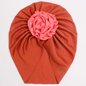 Ribbed brick red baby turban hat featuring a delicate pink fabric flower decoration