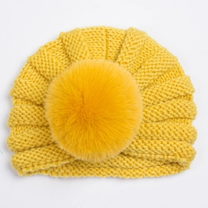 Détail d'un bonnet en tricot jaune vif pour bébé avec un grand pompon en fausse fourrure