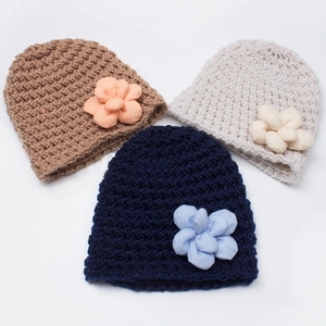 Close-up of three knitted baby hats in brown, white, and navy with large fabric flowers