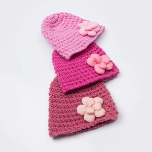 Detailed knit texture and layered flower ornaments on three crochet infant beanies