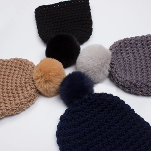 Close-up of four thick-knit baby winter beanies with large faux fur pom-poms in classic colors