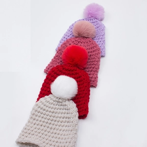 Detail showing various colors of thick knit beanies with fluffy faux fur pom poms