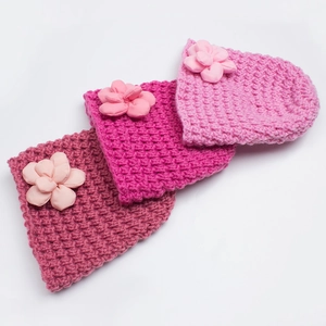 Detail of baby knitted beanies in pink shades featuring handmade 3D floral decorations
