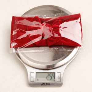 Bandeau bébé en velours rouge avec nœud pesé sur une balance affichant 25,4g