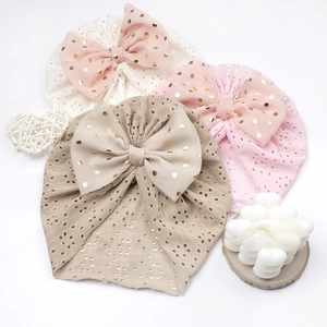Detail von Babymützen in Cremeweiß, Rosa und Khaki mit goldenen Chiffon-Schleifen