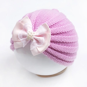 Détail du bonnet en tricot pour bébé avec grand nœud en satin, perles et dentelle