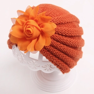 Détail du bonnet en tricot orange pour bébé avec une grande fleur en mousseline
