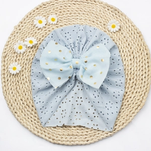 Detail von hellblauer Baby-Turban-Mütze mit goldener gepunkteter Schleife auf Strohmatte