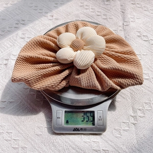 Macro shot of a camel ribbed baby beanie with cream flower detail showing 35.9g weight