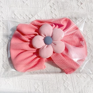 Detailed close-up of pink ribbed baby turban with a fabric flower in plastic packaging