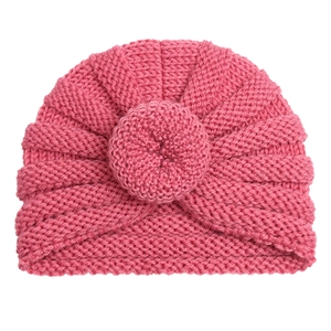 Detailed close-up of rose pink knit baby turban hat with decorative knot on white surface