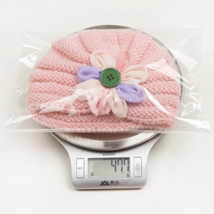 Pink knit baby beanie with colorful crochet flower detail and green button decoration