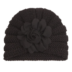 Détail d'un turban en tricot pour bébé avec une grande fleur noire décorative sur fond blanc