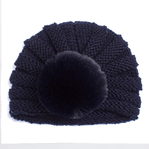 Détail du bonnet en tricot bleu marine pour bébé avec un grand pompon en fourrure