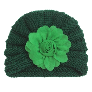 Détail d'un bonnet de naissance en tricot vert forêt avec une grande fleur en mousseline