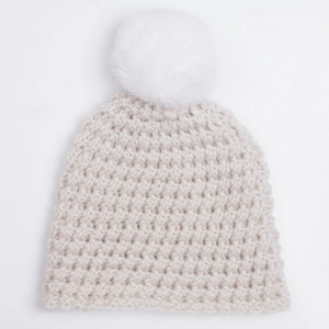 Close-up of beige knit baby hat featuring chunky texture and fluffy white faux fur pom-pom