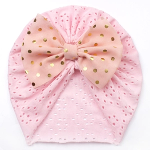 Detail der rosa gestrickten Babymütze mit großer Schleife und goldenem Punktmuster-Druck