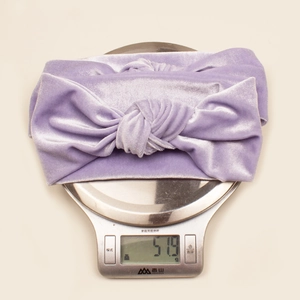Detailed view of light purple velvet knotted headband being weighed at 51.9g on a digital scale