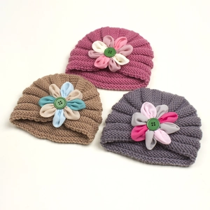 Close-up of three knitted baby turban hats with decorative flowers and button details