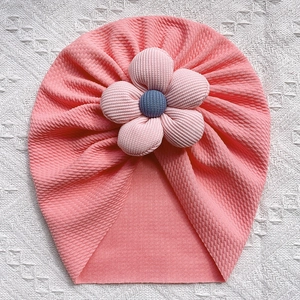Close-up of coral pink waffle knit baby turban hat with a large checkered fabric flower detail